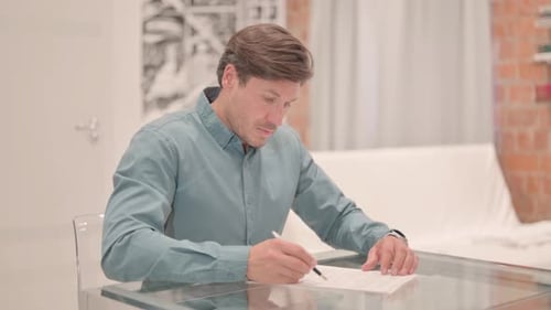 Man Signing Important Document at Home Desk