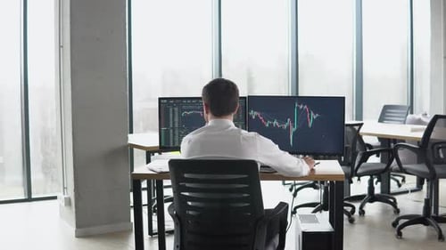 A visão traseira do Trader está trabalhando com várias telas de computador cheias de gráficos e análises de dados e