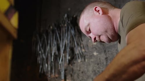 Slow motion side view of ironsmith forging wrought iron on anvil in workshop