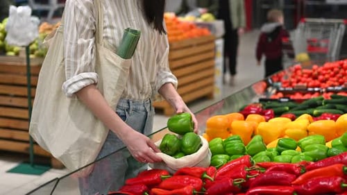 Mujer recogiendo pimientos en una bolsa reutilizable en una tienda. Temáticas del Día de la Tierra y la Ecología. Cámara lenta