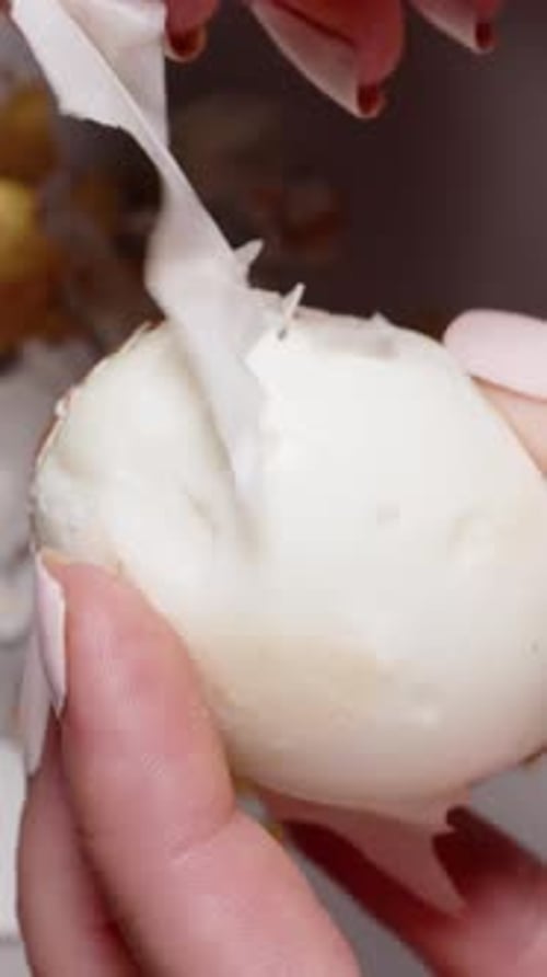 Vertical video. Hands peeling a hard-boiled Easter egg with golden fragments, revealing the white