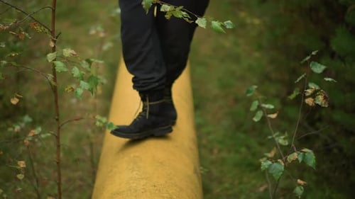 Boots Walking on Yellow Pipe in Grassy Field