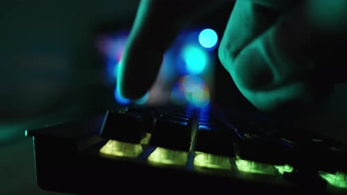 Dark room with rainbow lighting from the gaming PC, a keyboard where a finger is pressing a key.