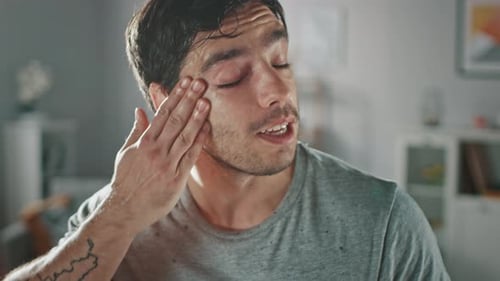 Sweaty Young Man Wipes Face Indoors in Close Up