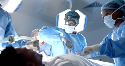Diverse surgeons wearing surgical gowns operating on patient in operating theatre, slow motion