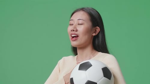 Side View Of Asian Woman With A Ball Singing National Anthem While Cheering Soccer On Green Screen