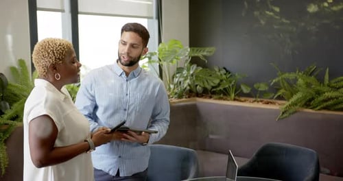 Smiling diverse colleagues holding tablets in modern office with indoor plants, copy space