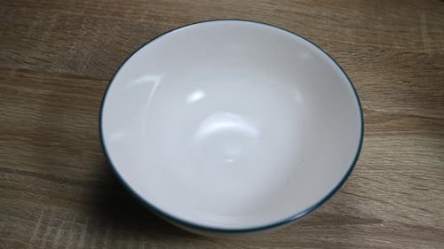 Empty bowl on a table, Granola poured in with a plastic container as part of a healthy breakfast.