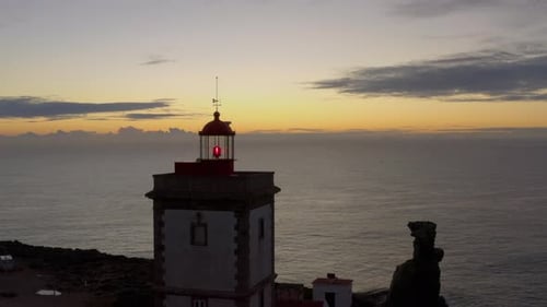 Aerial fly over coastal lighthouse with waves crashing on the cliffside.