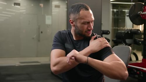 Adult Man Massaging Sore Shoulder in Gym