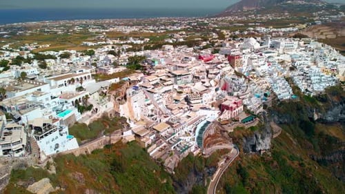 Aerial view towards buildings in a town, on the Santorini island, sunny evening, in Greece - Reverse