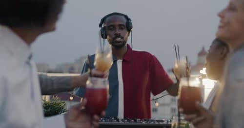 Estudantes felizes, homens e mulheres, batendo copos com DJ comemorando o feriado em uma festa na cobertura, curtindo