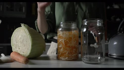 white housewife tightens the lid on a glass jar containing carrots and cabbage for fermentation