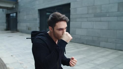 Young man training punch outdoor in slow motion on urban street workout