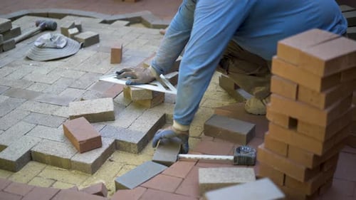 Bricklayer Building a Patio with Measuring Tools