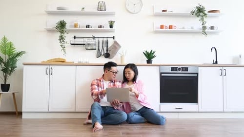 Couple in Kitchen Sitting Using Laptop Computer Indoors