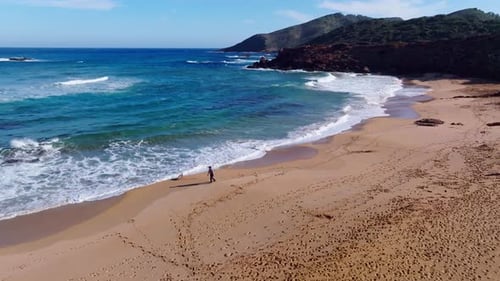 Cinematic aerial footage of person walking dog along the beach in Cala Pilar, Menorca Spain.