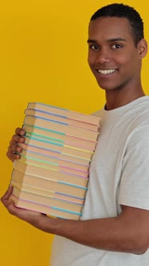 Smiling Student Boy Holding Academic Books Over Yellow Studio Background