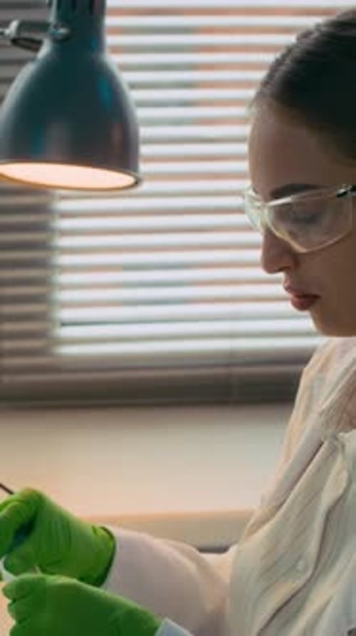 Vertical of Female Chemist Putting on Gloves and Mask in Laboratory