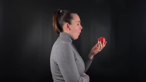 Woman Eats Red Apple Against Black Background