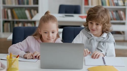Süße Klassenkameraden von Jungen und Mädchen, die zusammen am Laptop arbeiten und nacheinander den Test lösen, sitzen zusammen