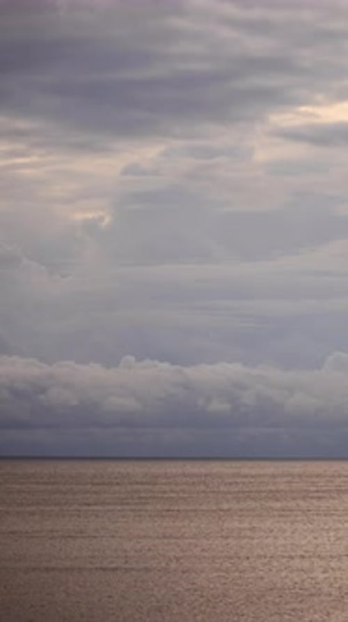 Vertical Timelapse of Sunrise Over the Sea with Golden Light Breaking Through Soft Layered Clouds