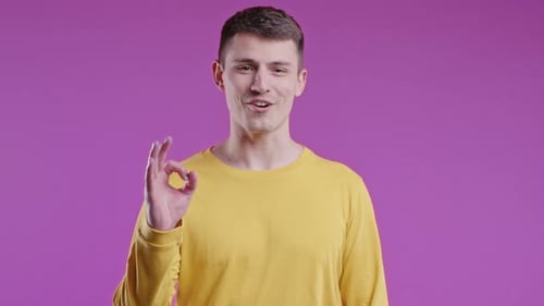 Positiver Mann macht OK Handzeichen Okay Geste Fröhlicher Student Guy im Pink Studio