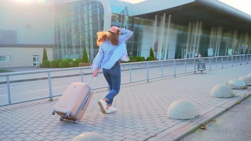 Young stylish girl hipster tourist runs a suitcase is late for departure to the airport or bus