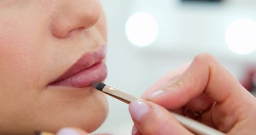 Nahaufnahme Professionelle Lippen-Make-up-Kosmetikerin trägt Lippenstift auf Schönes Frauengesicht Hand des Make-ups