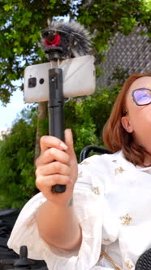 Content creator in wheelchair recording video with smartphone and external microphone