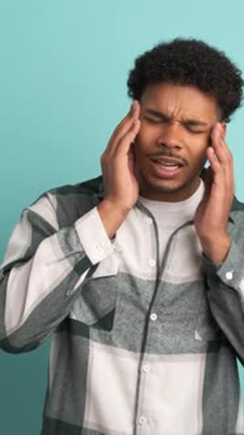 Frustrated Man Suffering From Headache in Blue Studio