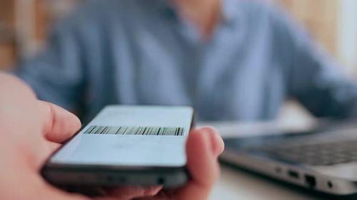 Scanning A Barcode On The Screen Of A Smartphone, A Buyer Client Shows An Employee To A Business