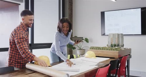 Happy diverse male and female architects with tablet discussing blueprints in office, slow motion