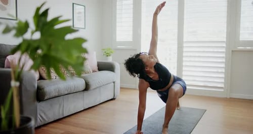 Mulher afro-americana em roupas esportivas agachada no tapete doméstico, estendendo o braço para cima para se equilibrar