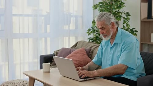 Senior Man Works on Laptop in Living Room
