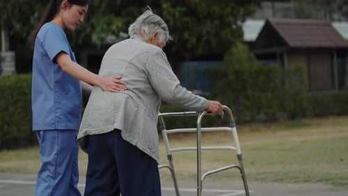 caregiver nurse support senior woman walking with walker in the park