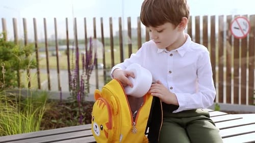 Un niño de primer grado se sienta afuera y abre un almuerzo de verduras