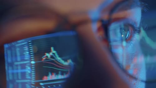 Trader Wearing Glasses is Working on Laptop Computer Screen with Stock Market Charts and Bitcoin BTC