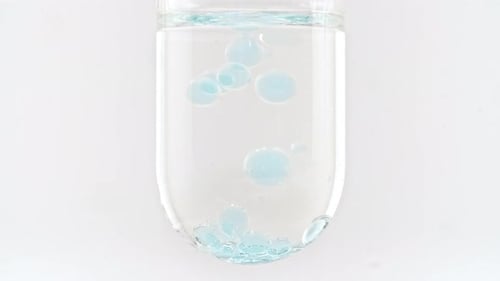 Foto macro de bolhas azuis de tamanhos diferentes descendo em tubo de ensaio de vidro sobre fundo branco