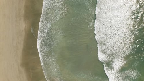 Aerial top view of turquoise sea waves approaching sandy beach on sunny day