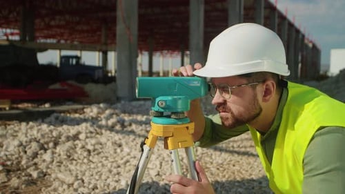 Side Shot of Bearded Focused Young Man Looking at Total Station Male Engineer Using Special