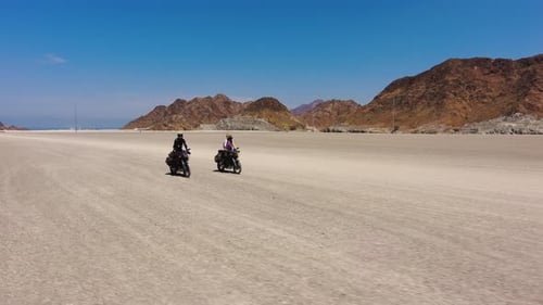 Adventure bikes ride on a flat off-road dirt track on a sunny summer day. Drone shot.