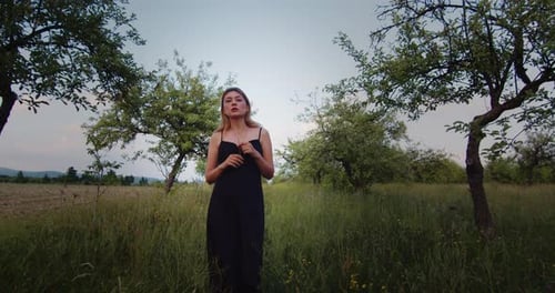 Beautiful female blonde model in black long dress walking in an apple garden