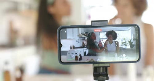 Mujeres afroamericanas filmando por teléfono en la cocina presentadoras que solicitan cuidado de la piel para un tutorial con biberones