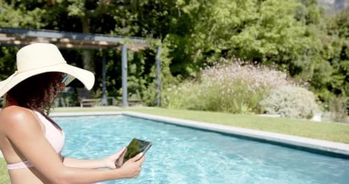 Relaxing by pool, woman in sunhat using tablet, enjoying summer day, copy space