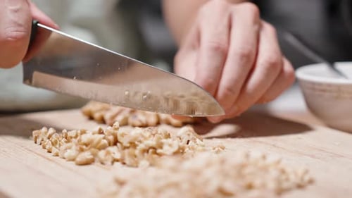 A woman is chopping walnuts with a knife in slow motion.