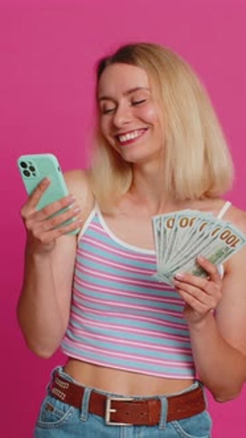 Smiling Woman Holds Phone and Money on Pink Background