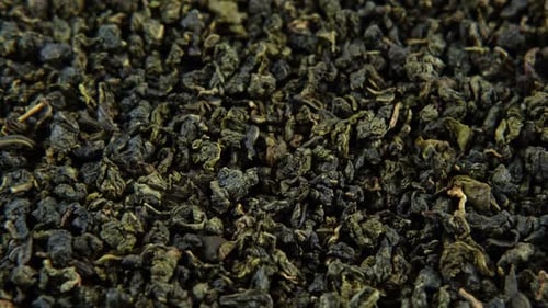 Schwarzer Trockentee-Tapetenmix aus schwarzen und grünen Teeblättern, rotierend auf einem Drehteller, Nahaufnahme, Makro, Ansicht von oben