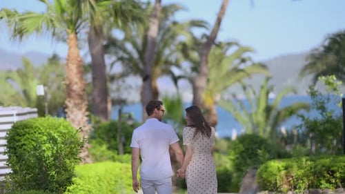 Couple walking hand in hand on a tropical path towards the blue ocean and palm trees