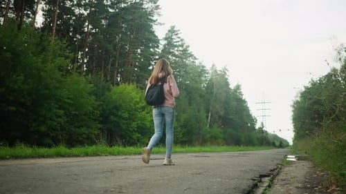 Young Woman Walking on Rural Road Surrounded By Green Forest